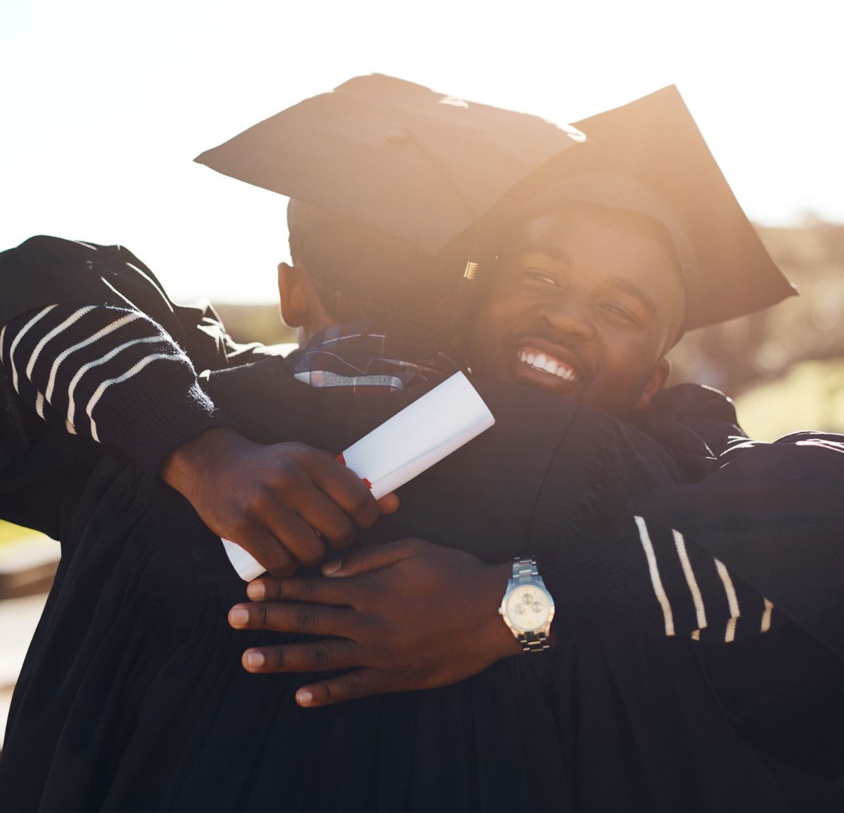 Black male college grads in cap and gown hug